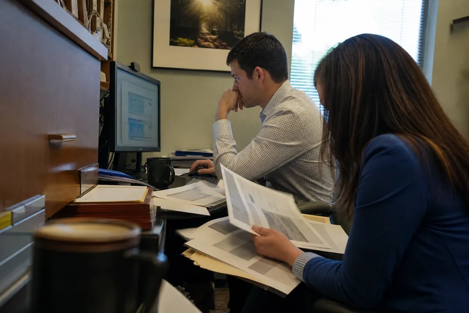 Two accountants reviewing monthly statement volume next to stacks of client bank statements
