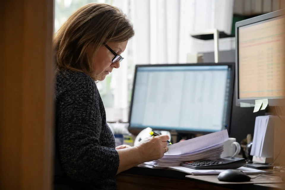 Bookkeeper comparing a spreadsheet export with a ledger on two monitors in a small office
