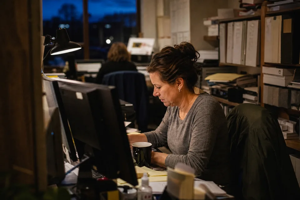 Bookkeeper working late at a two-monitor desk in a small accounting office