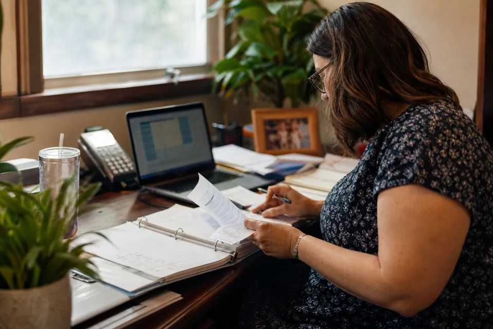 Nonprofit finance manager reconciling a bank account from printed statements beside a laptop